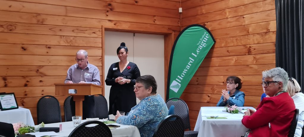 People in a room sitting at tables with a man giving a speech at a lectern. 